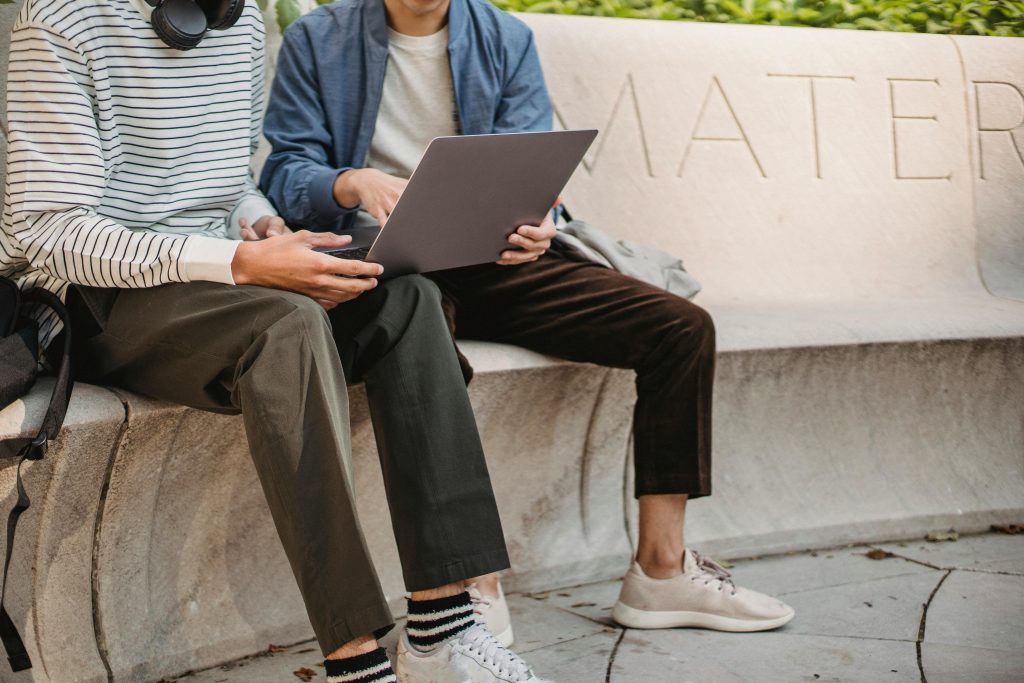 two man sitting on stone bench with laptop